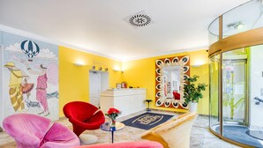 A hotel lobby with a reception desk, a large mirror, a red chair, and a colorful mural on the wall. - Hotel Europa (Brno)