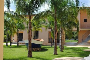 A courtyard with palm trees, a boat, and a building with a staircase. - Hotel Residence Aquilia (Badolato Marina)