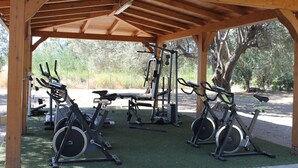 Un espace de remise en forme extérieur abrité, équipé de vélos d’appartement, d’un banc et de matériel de musculation.