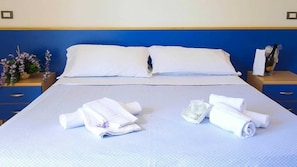 Un lit bien fait, avec des draps blancs, deux oreillers et un ensemble de serviettes posé sur une couvre-lit bleue et blanche.