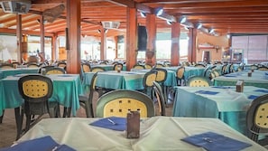 Un amplio comedor interior con varias mesas cubiertas con manteles verdes y sillas con respaldos amarillos.
