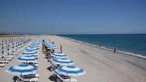Ein Strand mit Liegestühlen und Sonnenschirmen, einem klaren Himmel und dem Ozean im Hintergrund.