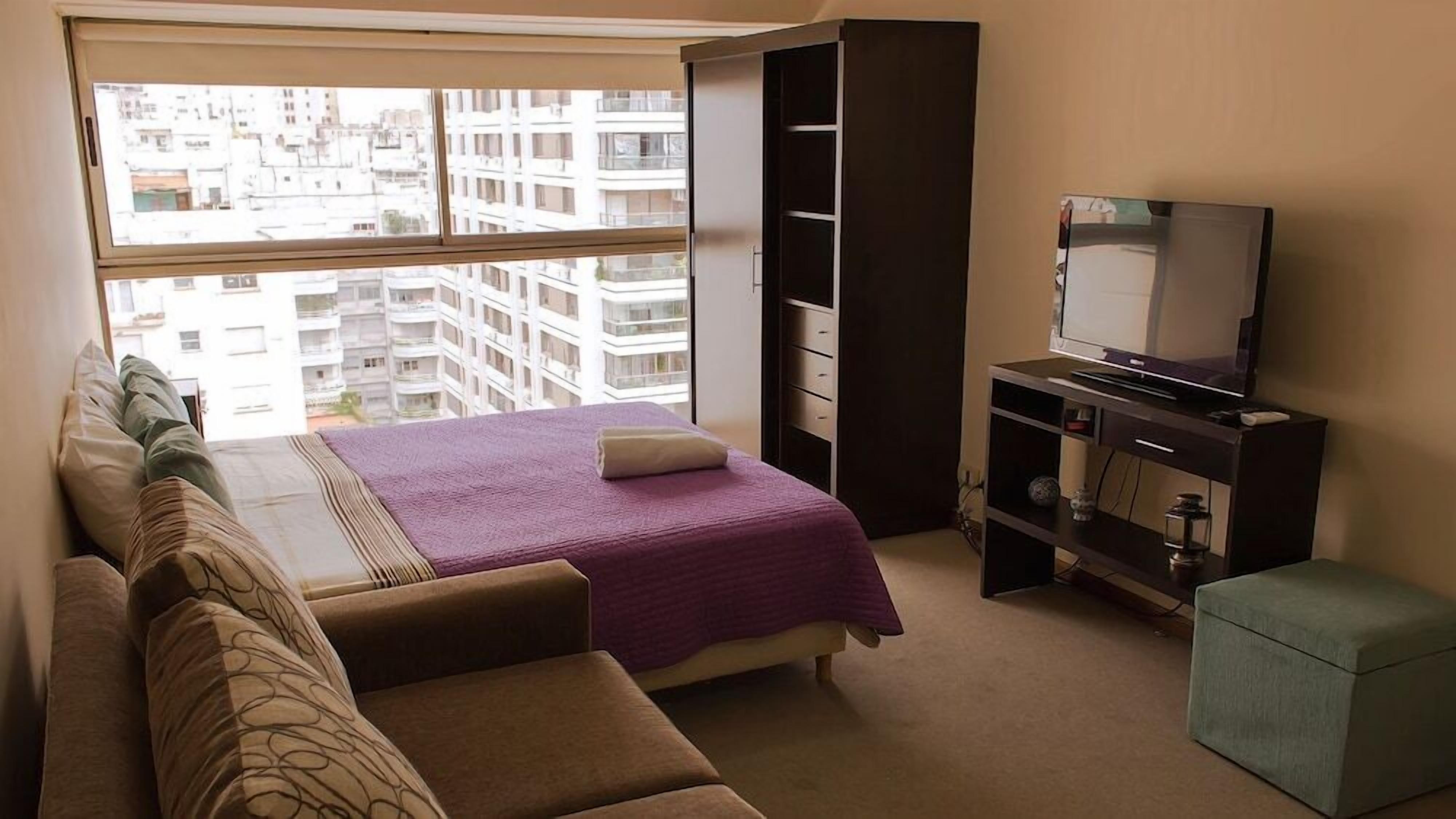 Una camera da letto con un letto, un divano, una TV e una finestra vista città.