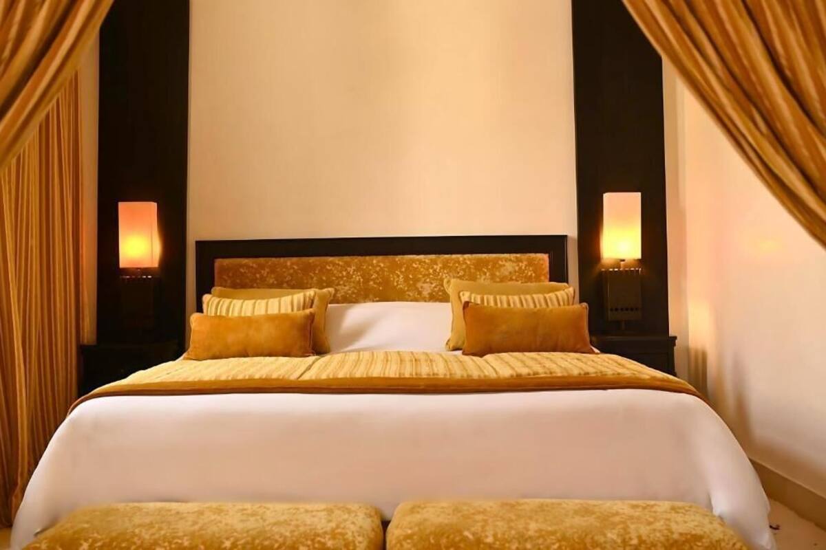 A large bed with a white headboard and multiple pillows, flanked by two wall-mounted lamps.