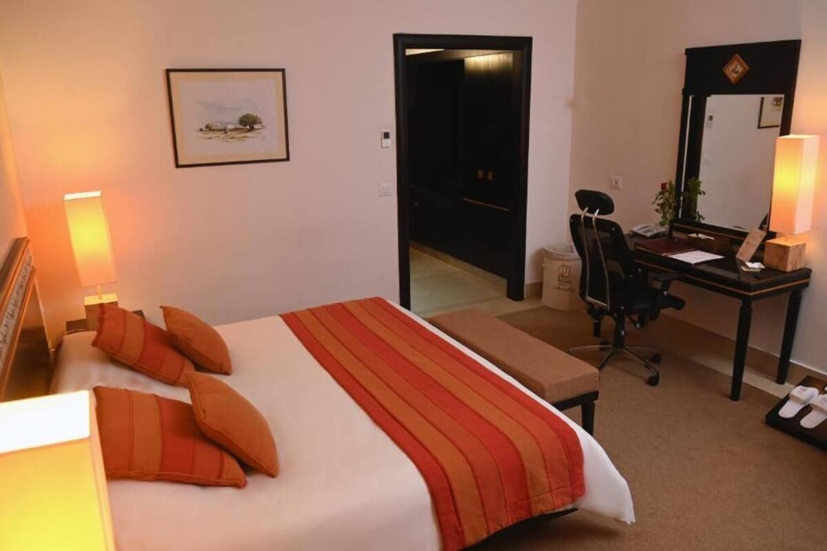 A hotel room with a bed, a desk, a chair, a mirror, and a door leading to another room.