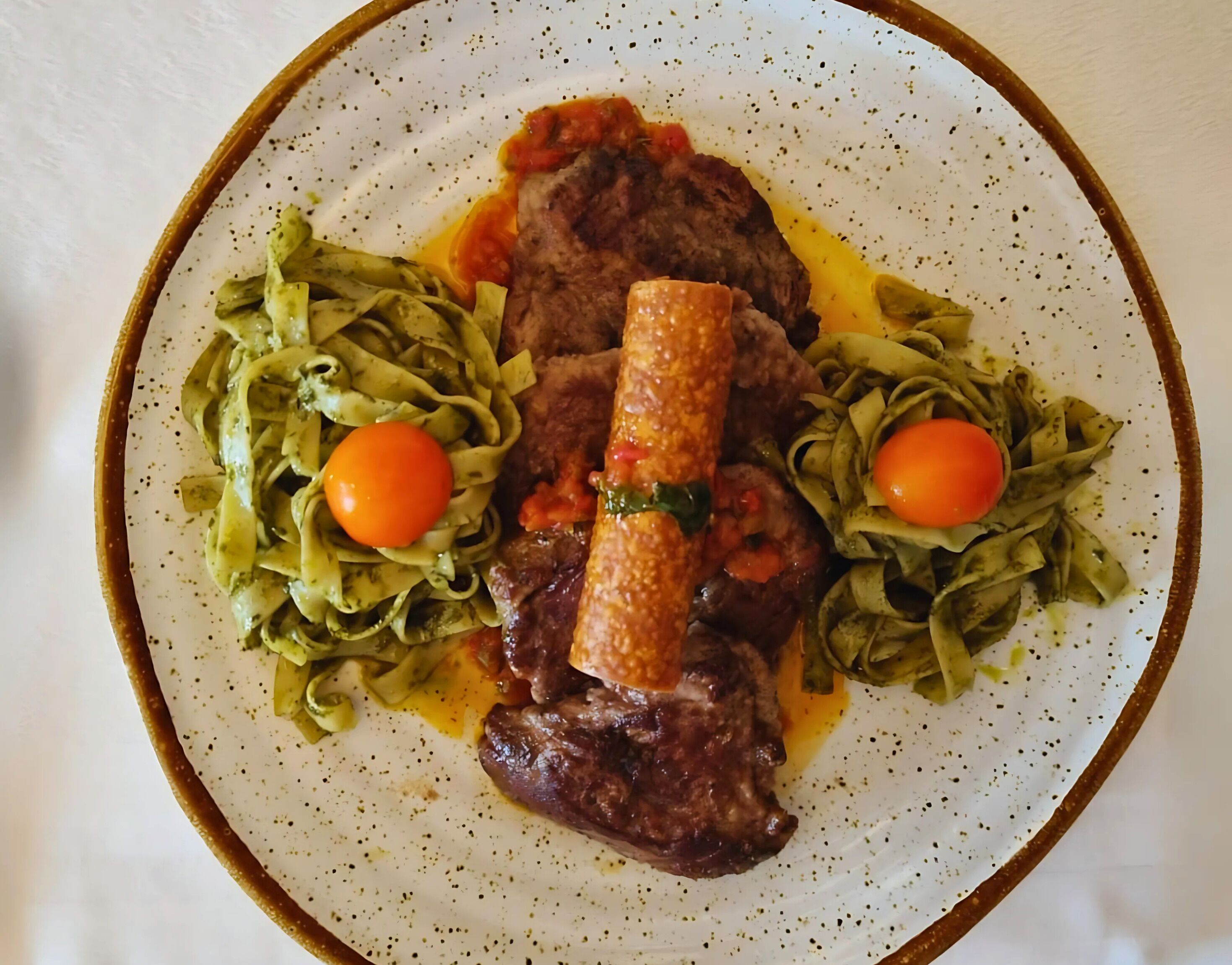 Une assiette de nourriture comprenant un plat de viande, des pâtes et deux tomates cerises.