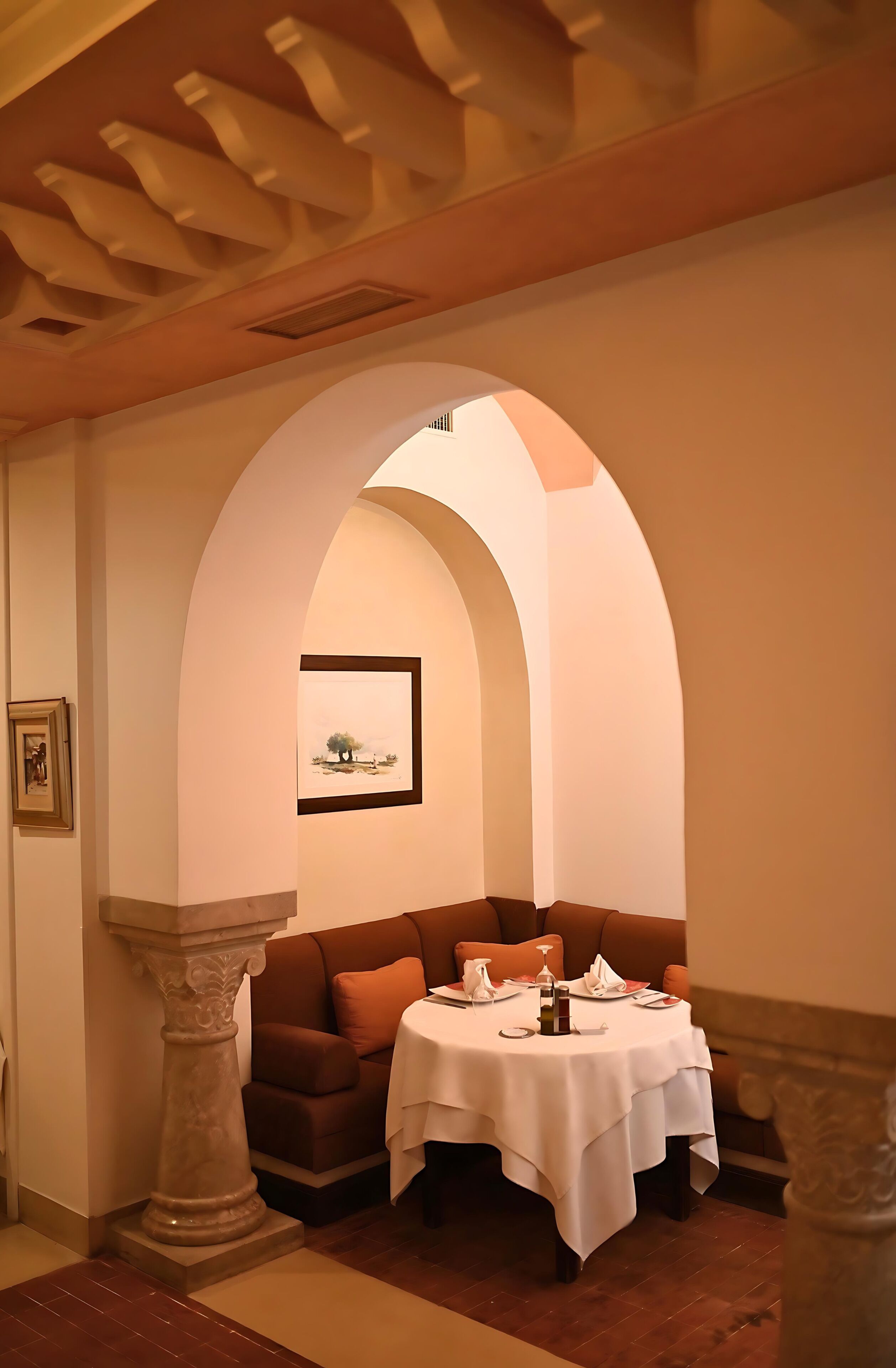 A dining area with a table set for two, a cushioned bench, and a framed artwork on the wall.