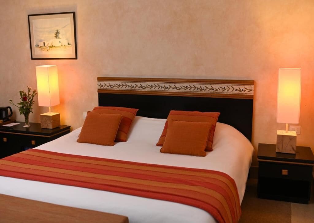 Een hotelkamer met een groot bed, twee nachtkastjes, een lijst aan de muur en twee bedlampjes.
