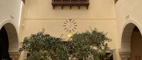 Un amplio atrio con un gran árbol, varias zonas de estar y un reloj en la pared.