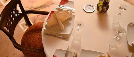 A round dining table with a white tablecloth, neatly set with plates, cutlery, and wine glasses.