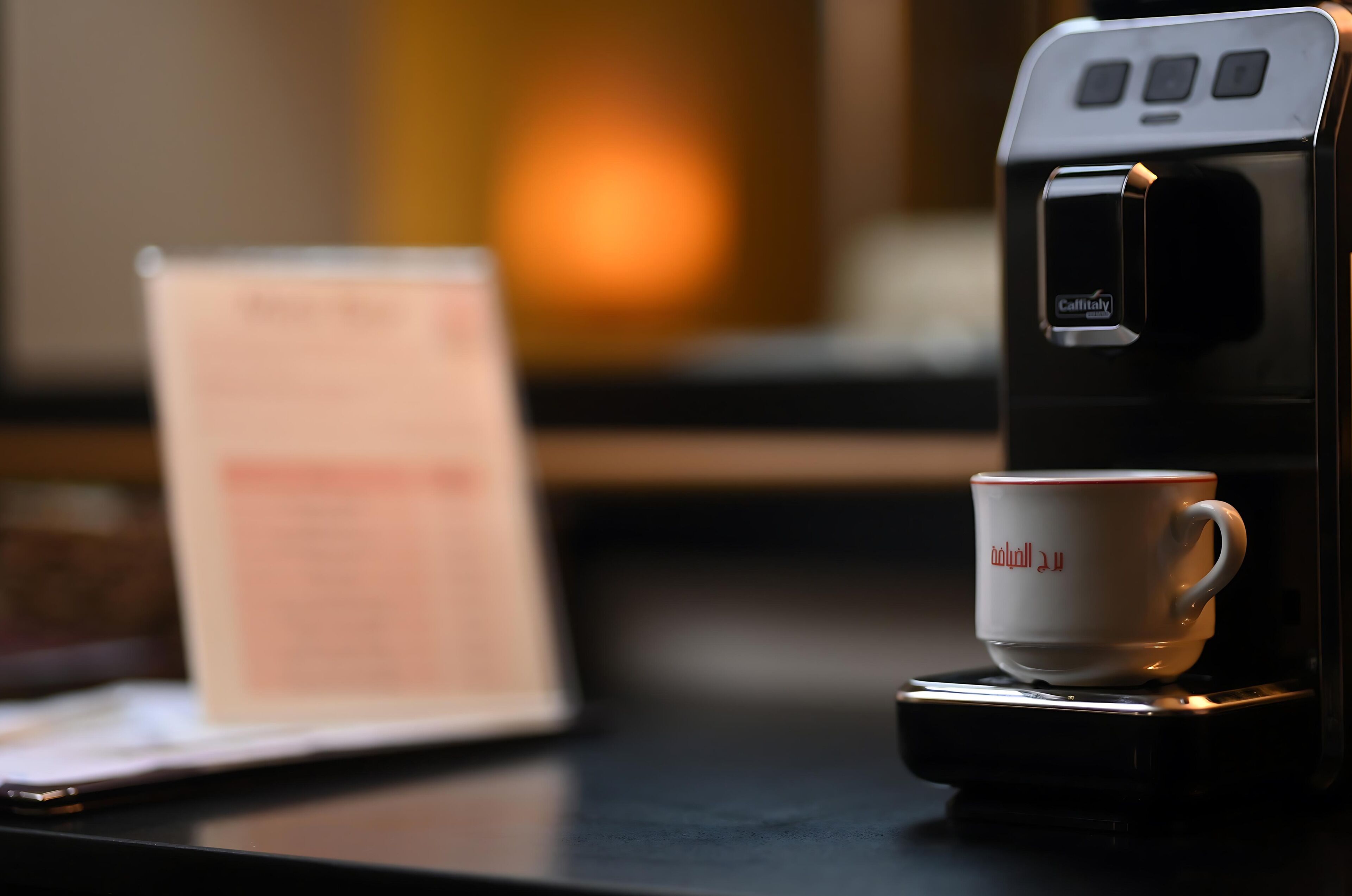 A coffee machine with a cup on its base, a laptop, and a blurred background.