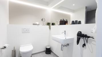 A modern bathroom with a white sink, a toilet, a trash can, and a hairdryer on the wall.