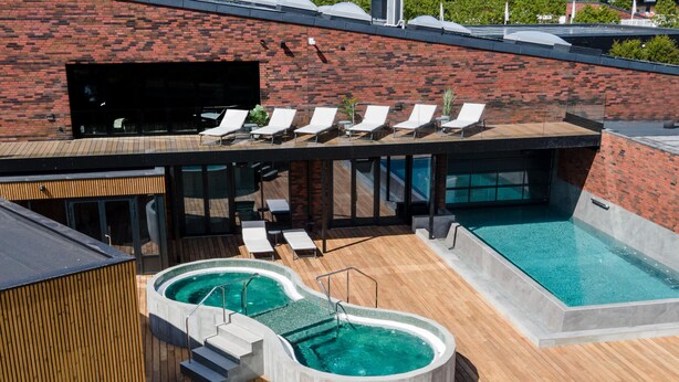 A rooftop pool area with two hot tubs and lounge chairs.