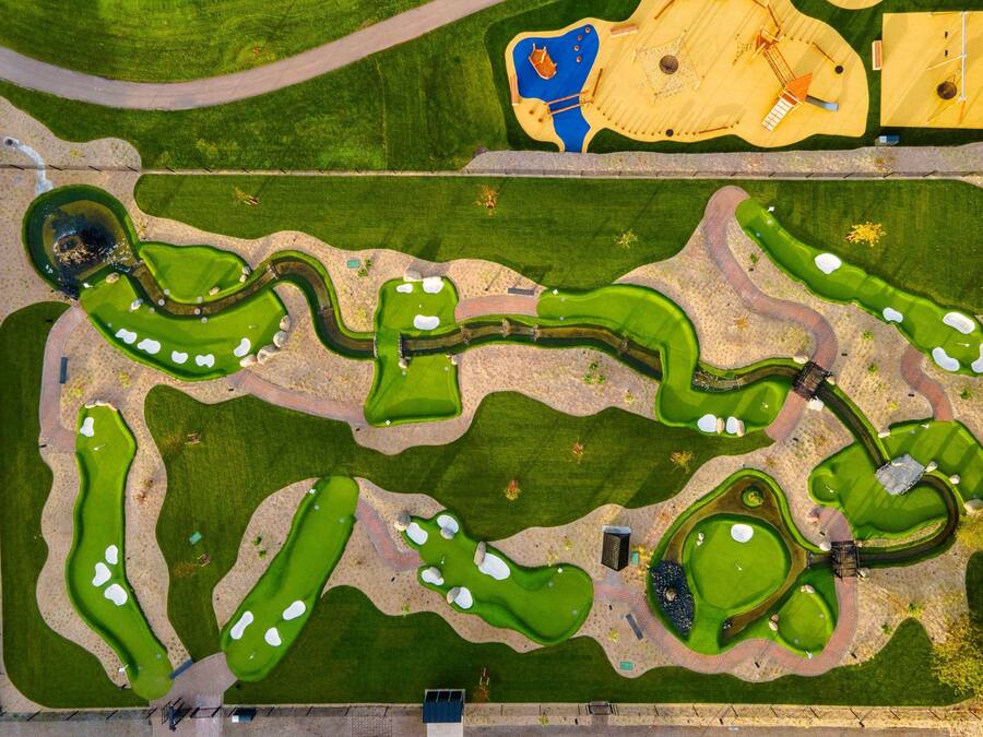 An aerial view of a golf course with multiple greens, bunkers, and a water hazard.