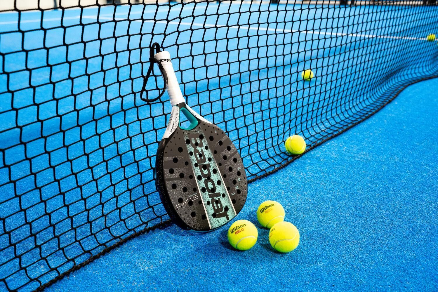 Ett tennisracket lutat mot nätet, med tennisbollar på en blå tennisbana.