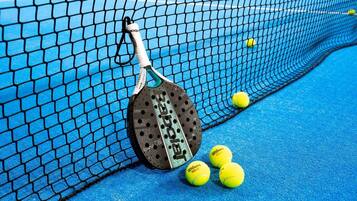 Ett tennisracket lutat mot nätet, med tennisbollar på en blå tennisbana.