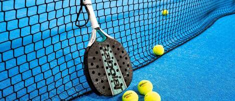 A tennis racket leaning against a net with tennis balls on a blue court.