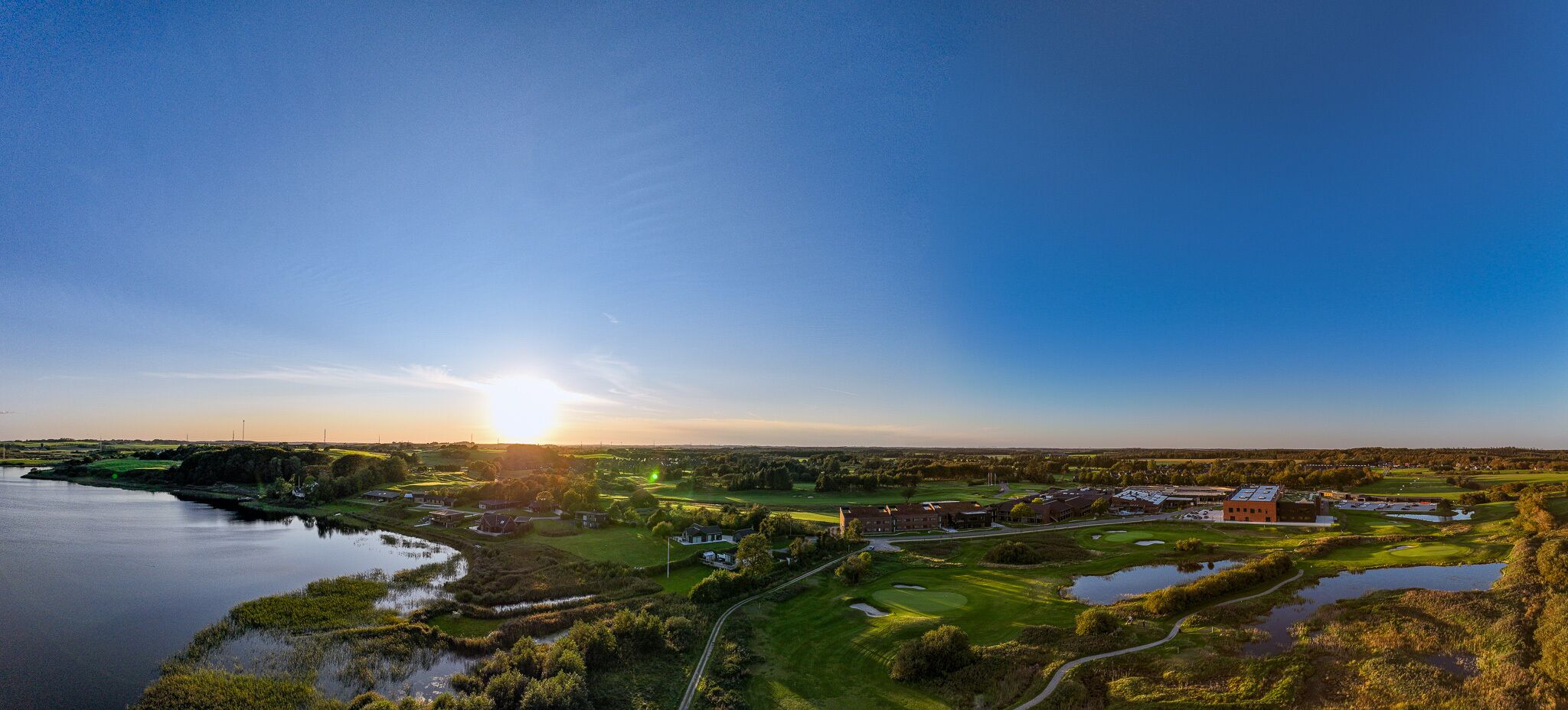 Un campo de golf con un edificio grande, una masa de agua y un cielo despejado.