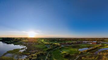 Un campo de golf con un edificio grande, una masa de agua y un cielo despejado.