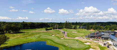 A golf course with a pond, a clubhouse, and a parking area.