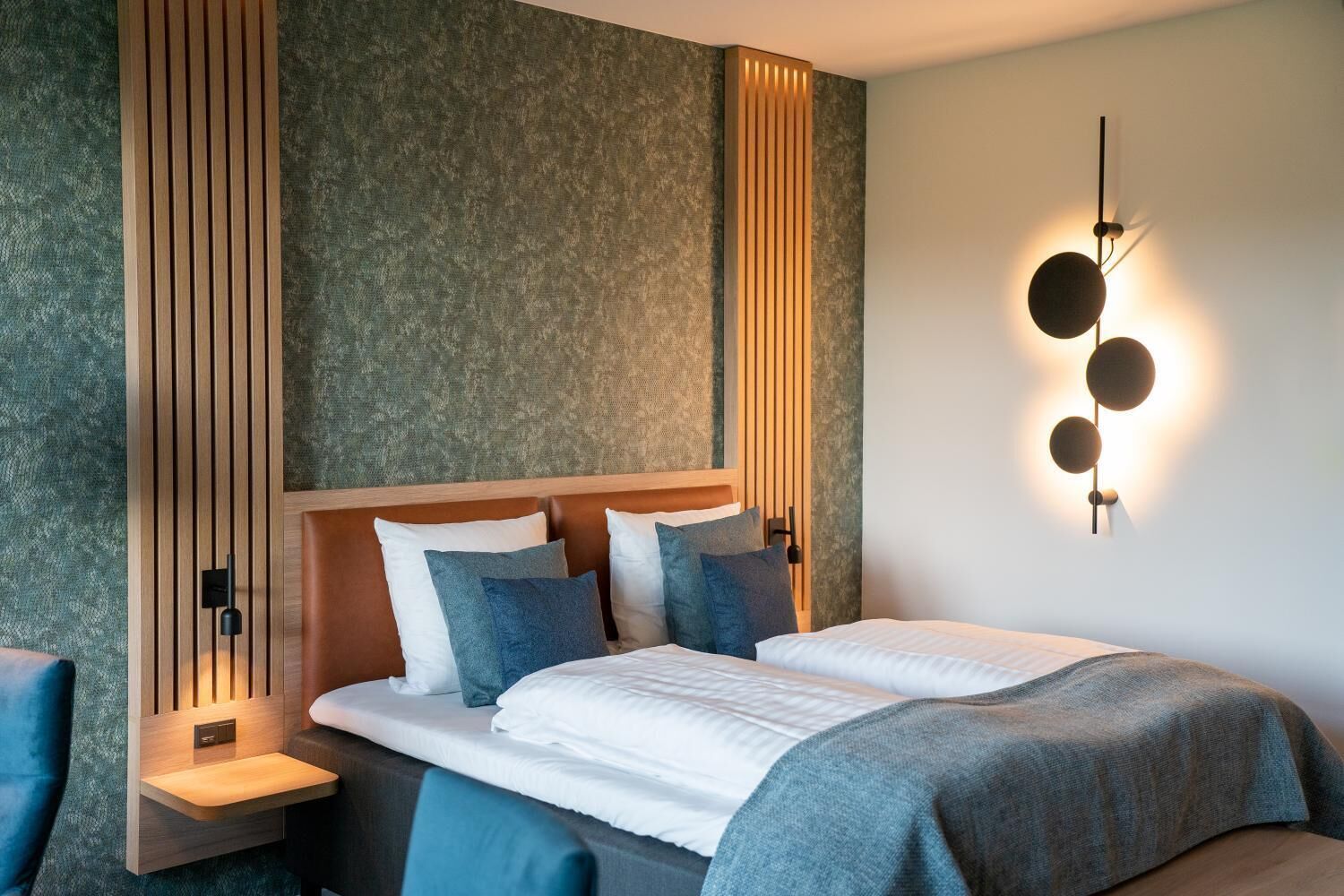 A modern bedroom with a bed, bedside tables, and a wall-mounted light fixture.