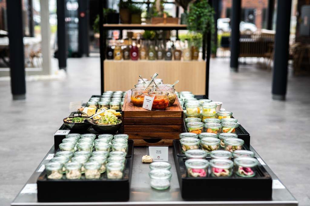 Une présentation de produits alimentaires comprenant divers pots contenant différents aliments, un comptoir en bois et un décor composé d’étagères et de plantes.