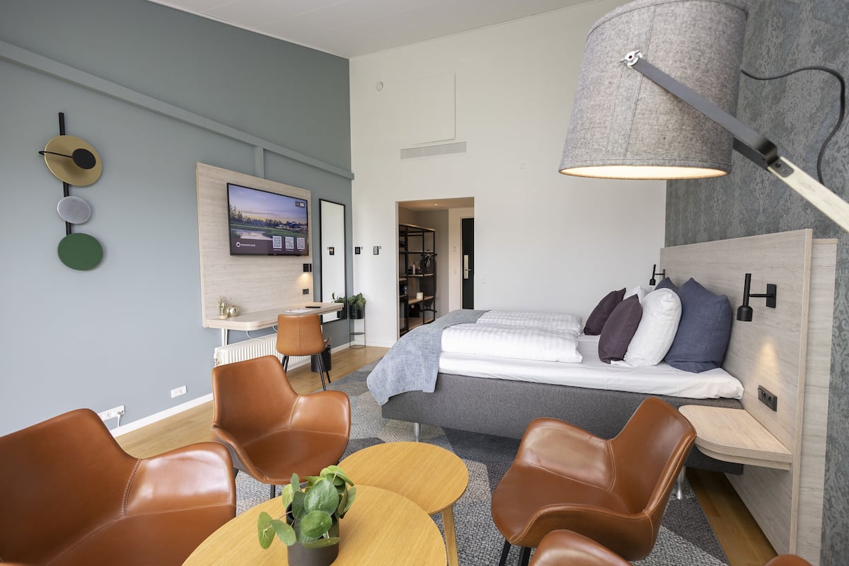 Et moderne hotelværelse med seng, skrivebord og siddeområde med stole og et bord.