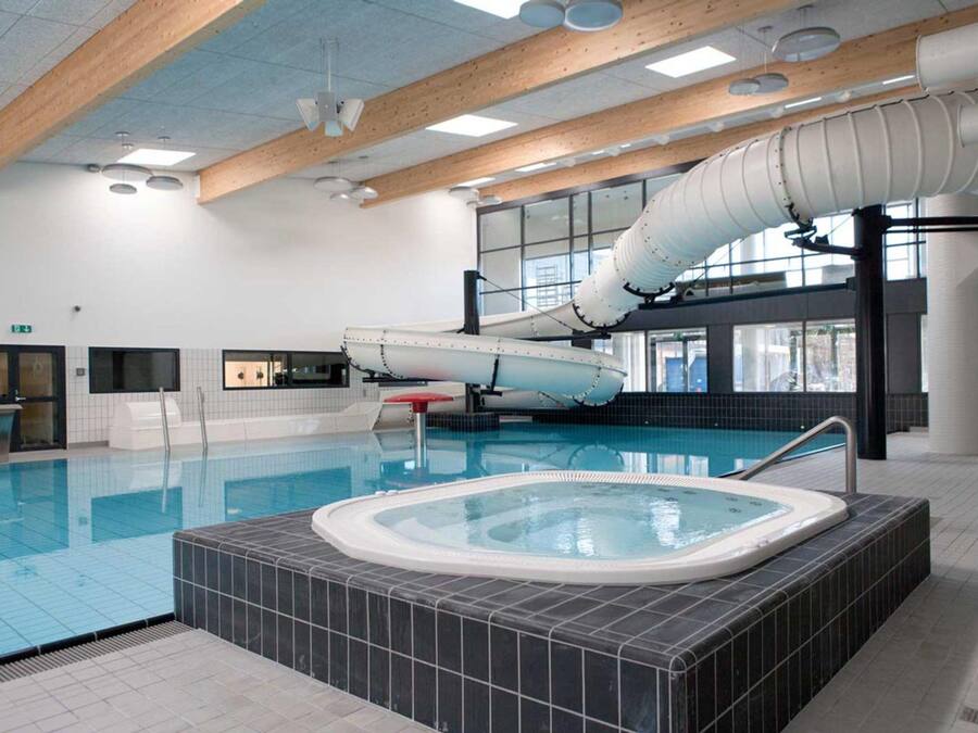 En indendørs swimmingpool med jacuzzi, træbjælker og et stort vindue.