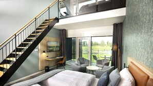 A modern hotel room with a staircase, a bed, a desk, and a balcony with a view of the outdoors.