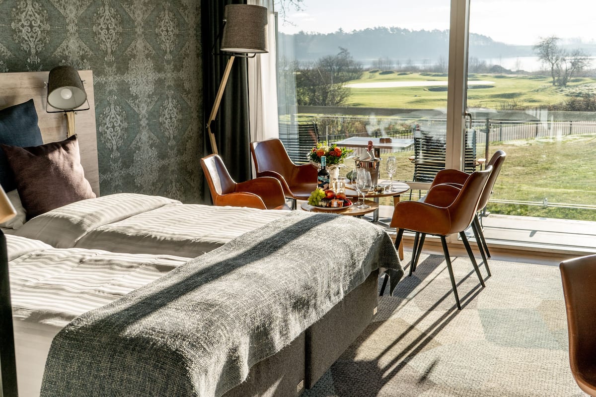 Et soveværelse med en stor seng, et spisebord med stole, udsigt til en golfbane og en lampe.