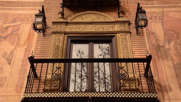 Un balcón con barandillas de metal ornamentadas y suelo a cuadros.