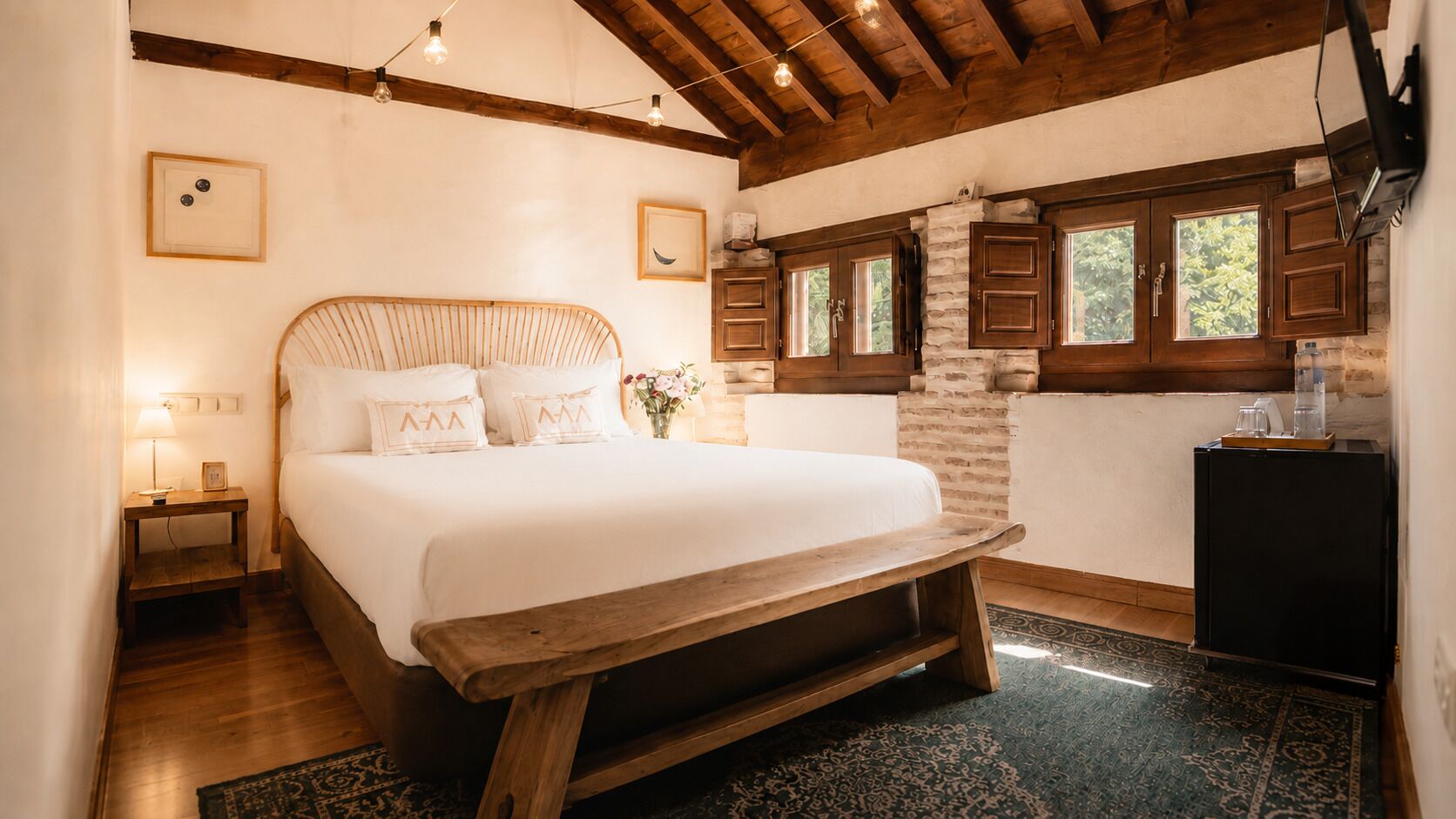 A bedroom with a bed, wooden headboard, bedside tables, a bench, a nightstand, a dresser, and a window with wooden shutters.