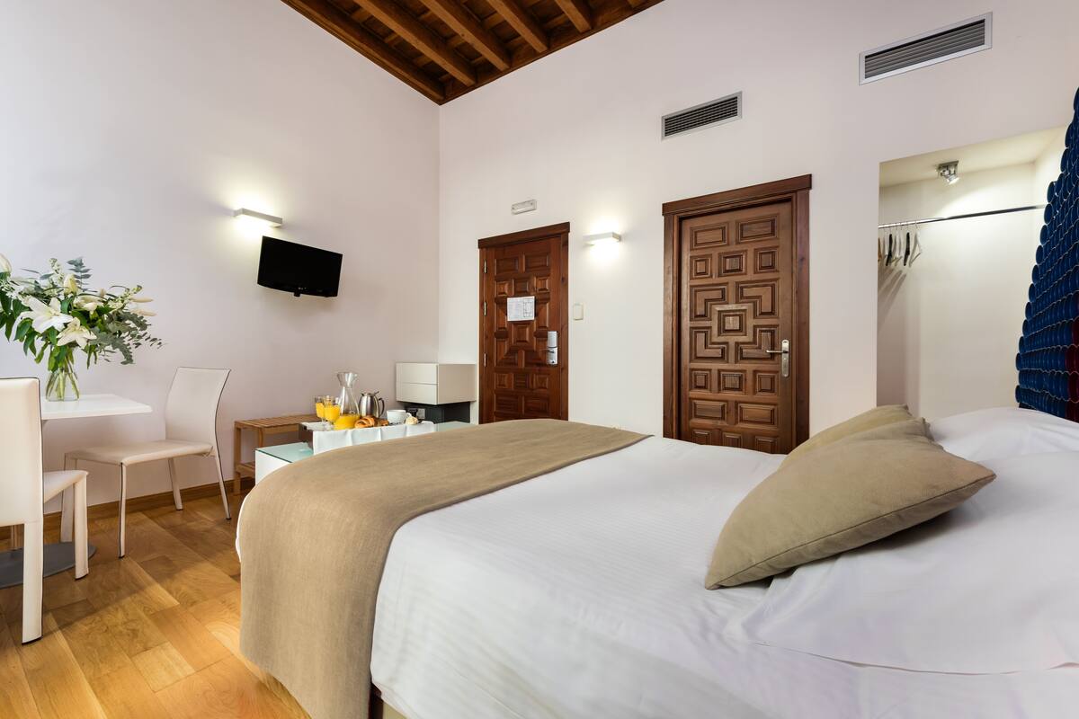 A hotel room with a bed, a desk, a chair, a TV, and a door.