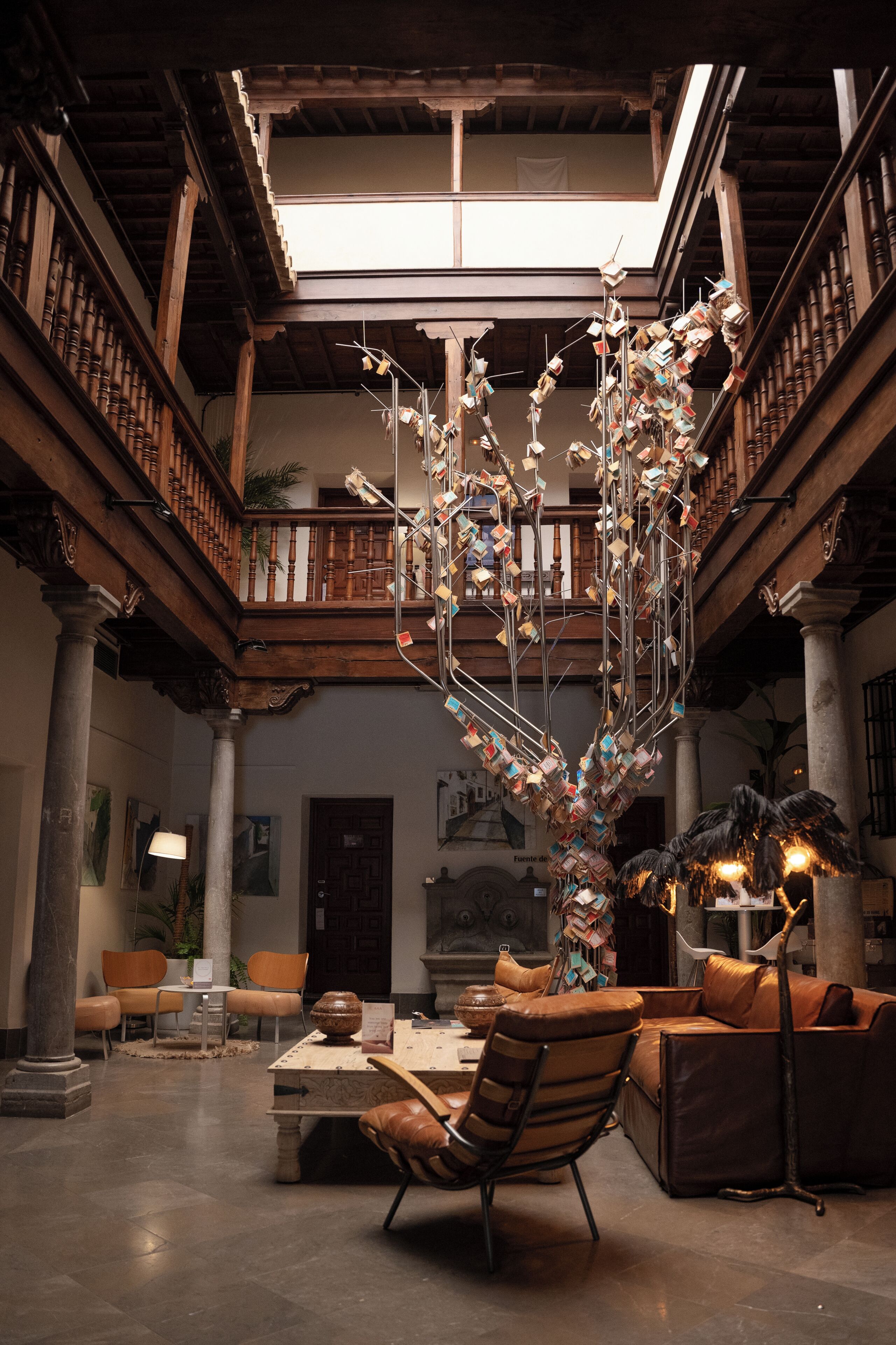 A spacious atrium with a high ceiling, wooden balconies, and a central column with a decorative metal sculpture.