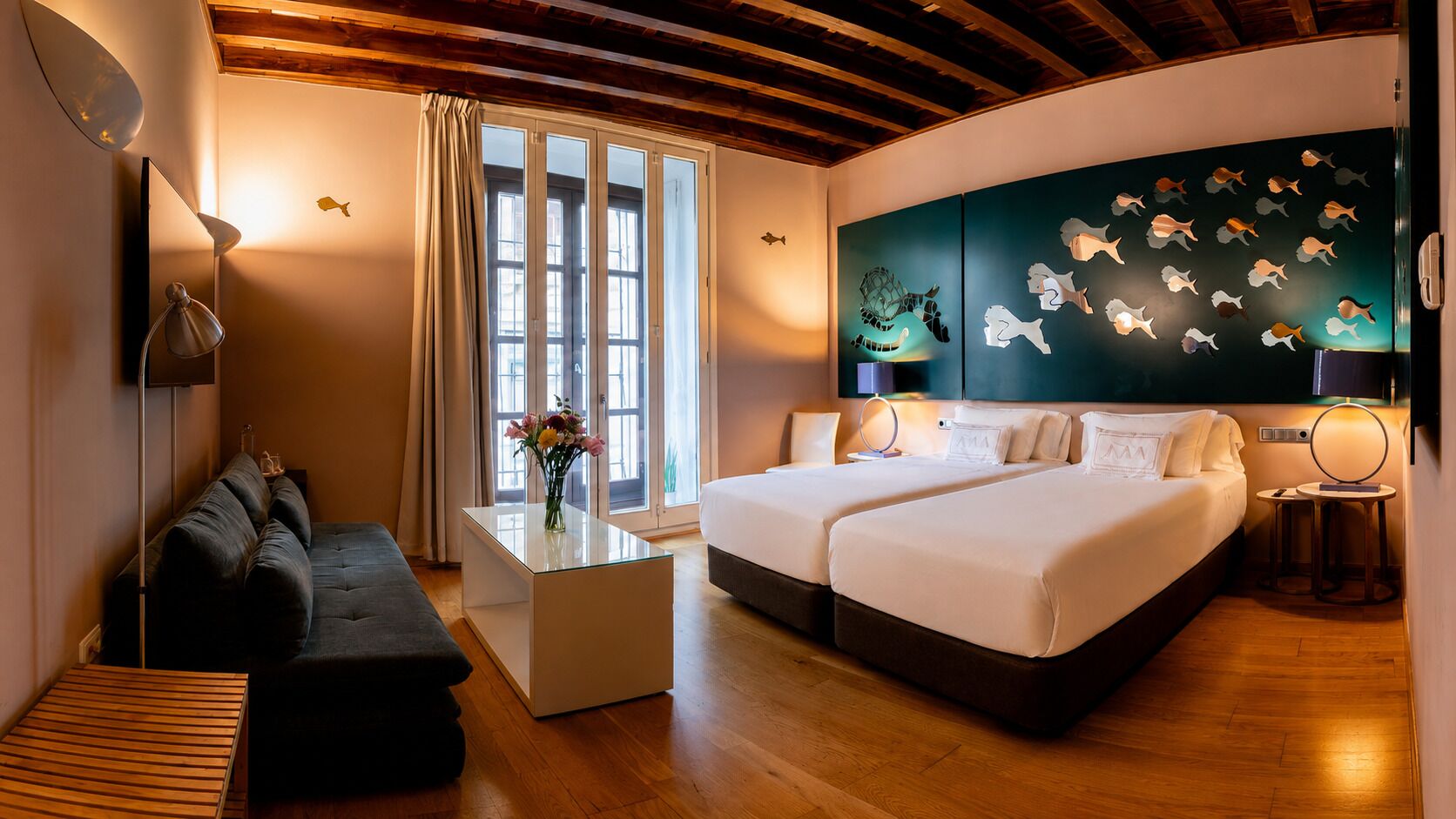 Une chambre d’hôtel avec un lit, un canapé, une table basse et un mur décoré de motifs représentant des poissons.
