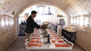 A long table set with red napkins, clear glassware, and a vase with flowers, in a brick-walled corridor with a kitchen in the background. - Gar Anat Hotel Boutique - Domus Artis.  (Granada)