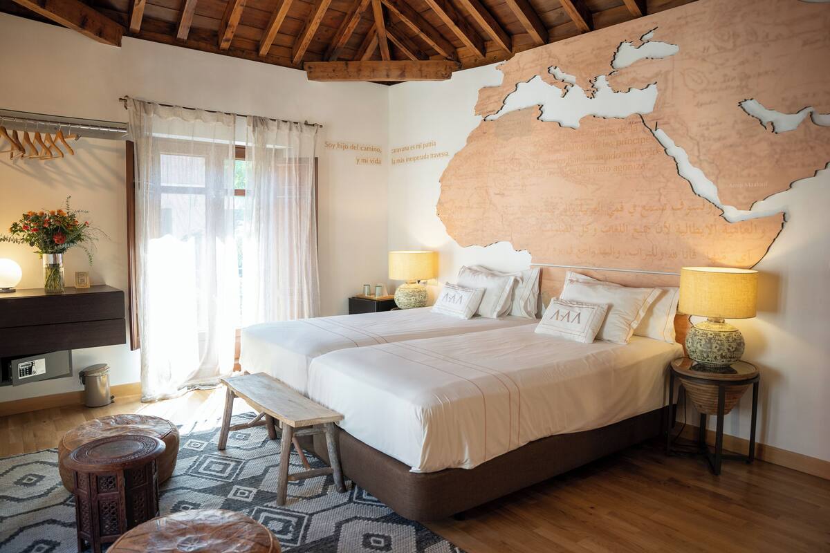 A bedroom with two beds, a map on the wall, a wooden ceiling, and a window with curtains.