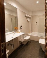 A modern bathroom with a double sink, a toilet, a bathtub, and a glass shower enclosure.