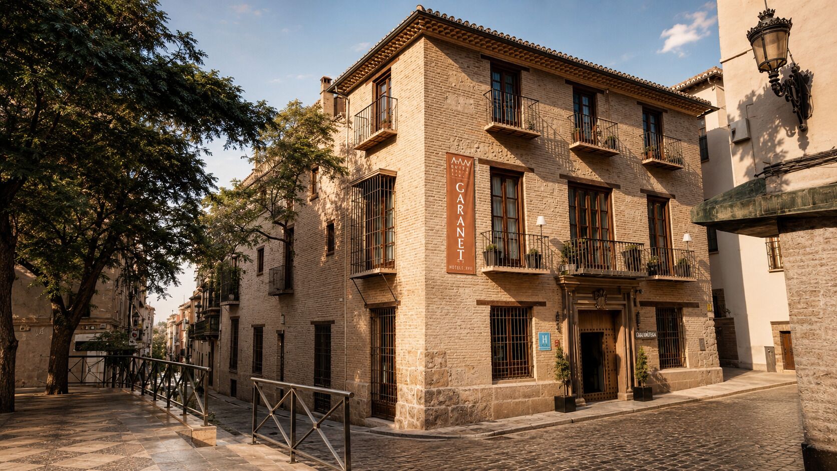Un hotel con fachada de piedra, varios balcones y una calle adoquinada.