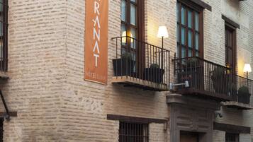 Fachada de hotel con un cartel llamativo, balcones con plantas y un paseo peatonal.