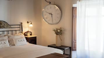 Un dormitorio ordenado con cama, mesita de noche, lámpara, reloj y un florero con flores.
