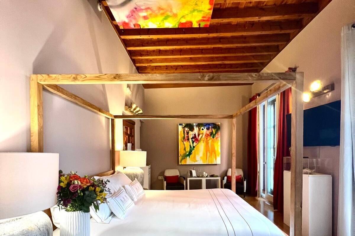 A modern bedroom with a wooden bed frame, a large painting above the bed, and a wooden ceiling.