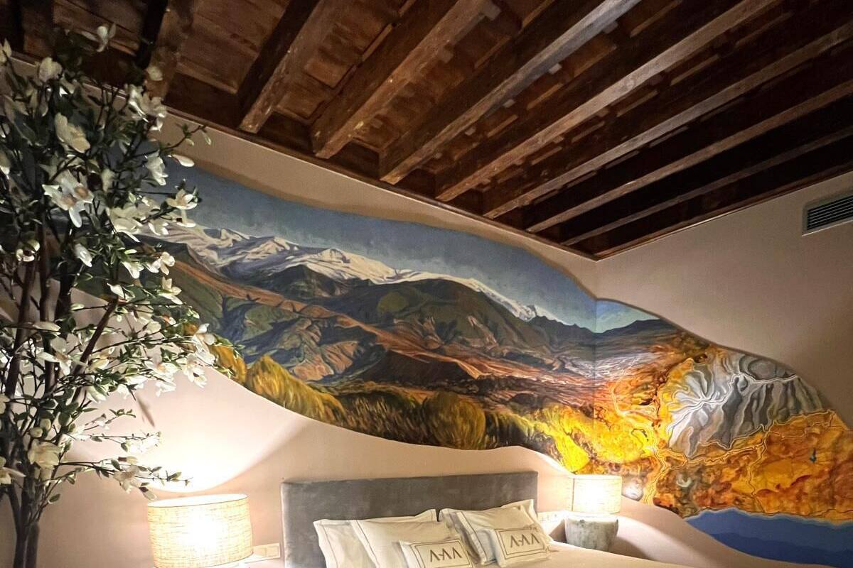 A bedroom with a bed, nightstands, a potted plant, and a mural on the wall.