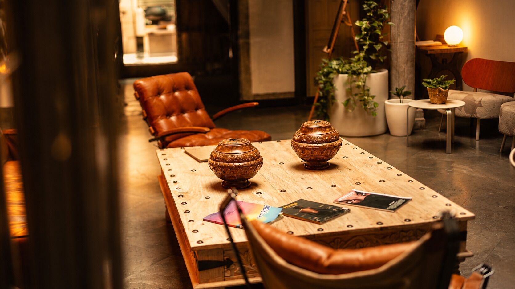 Una mesa de madera con dos cuencos decorativos, una silla de cuero y una pequeña mesa con plantas.