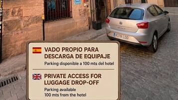 Entrada de hotel con un letrero que indica acceso privado para dejar equipaje y un coche estacionado adelante.