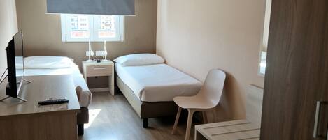 Quarto moderno e compacto com cama, escrivaninha, cadeira e uma mesinha.