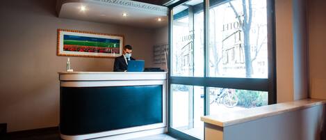 A hotel reception desk with a large window, a framed painting, and a modern interior design.