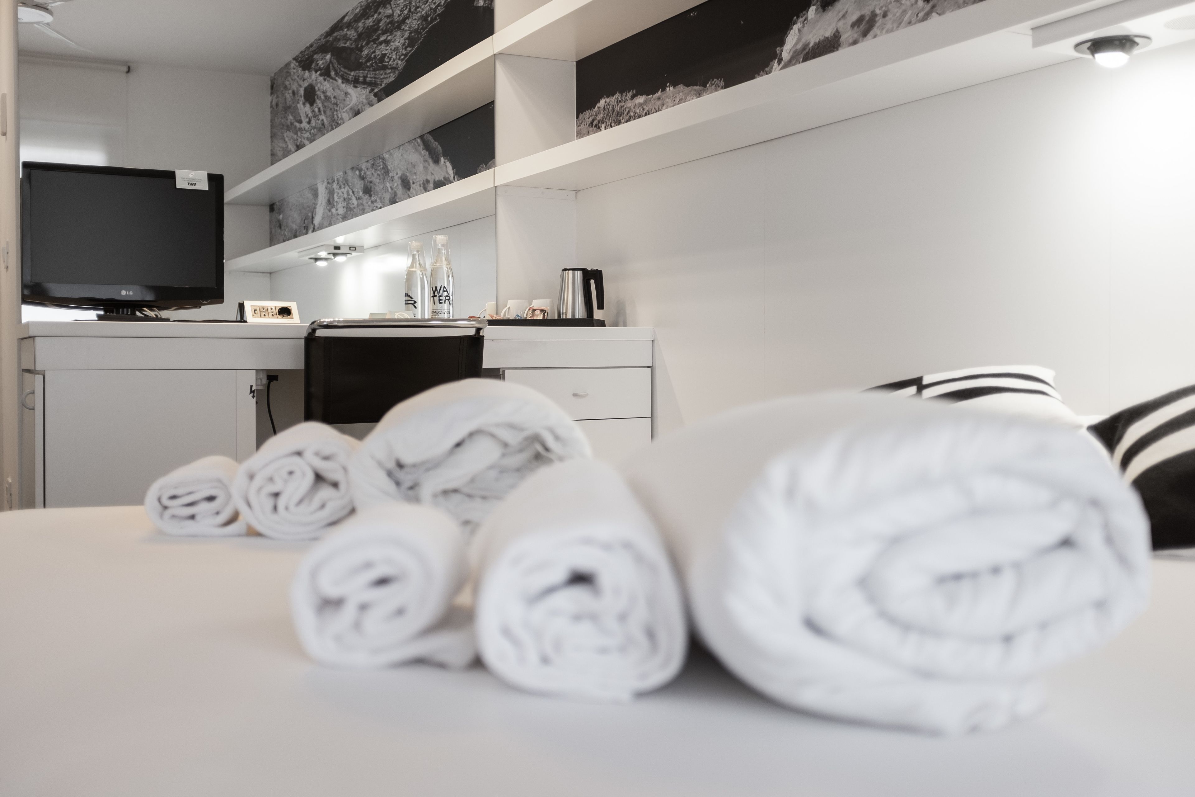 A modern hotel room with a neatly made bed, a flat-screen TV, a coffee maker, and a minibar.