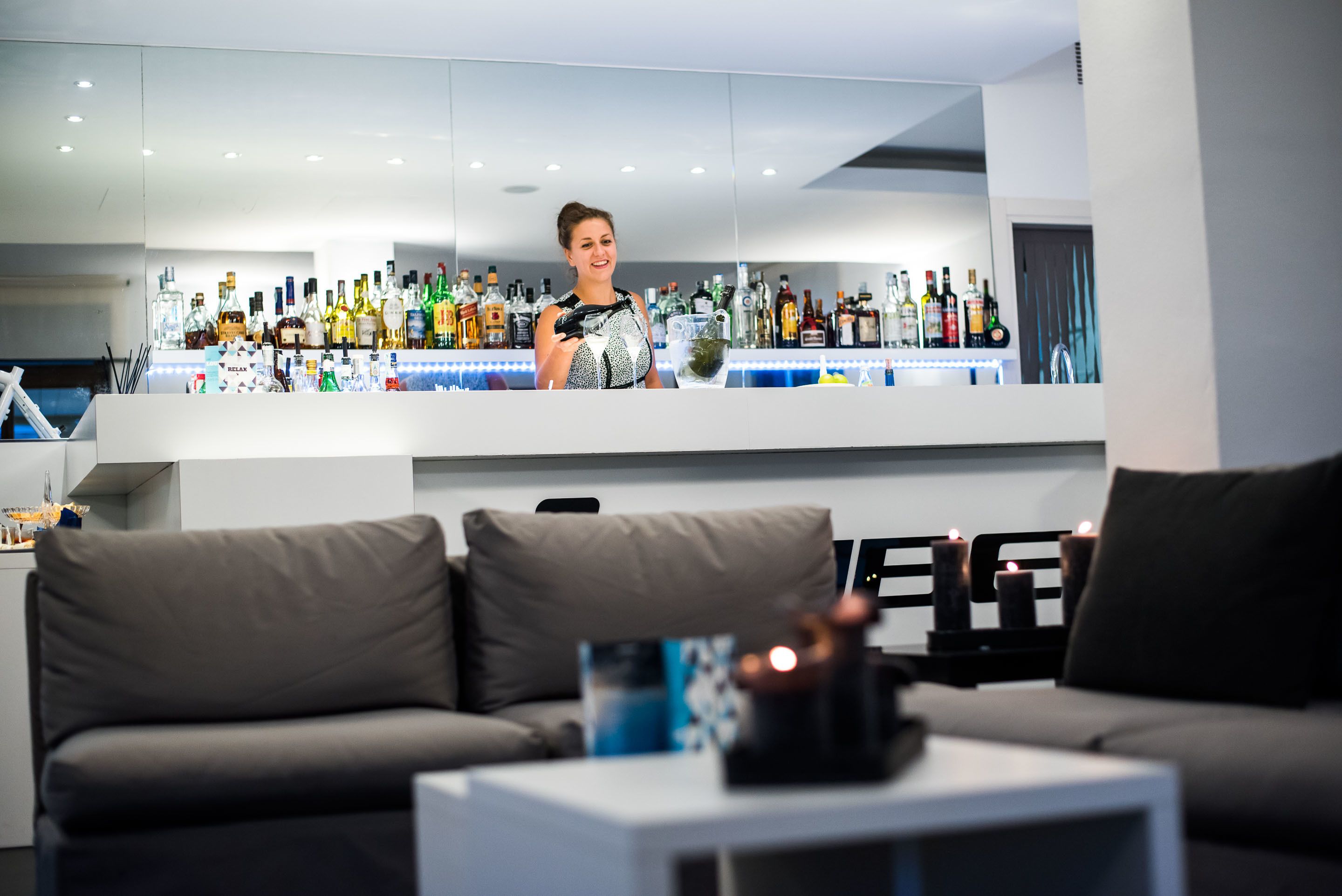 A modern bar area with a variety of liquor bottles, a bar counter, and a seating area with a sofa and a coffee table.