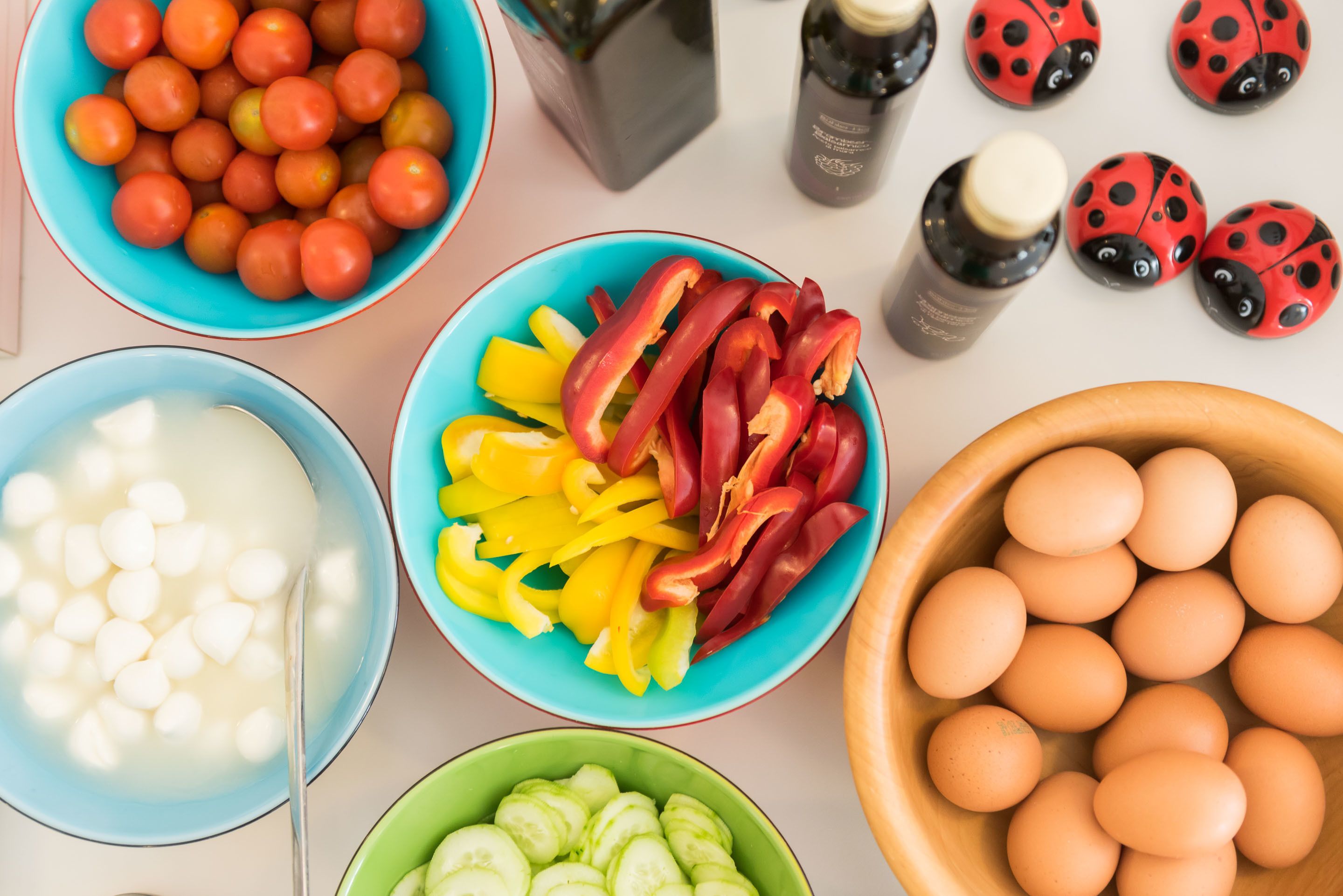 Kommetjes met diverse ingrediënten, zoals tomaten, paprika's, komkommers en eieren.